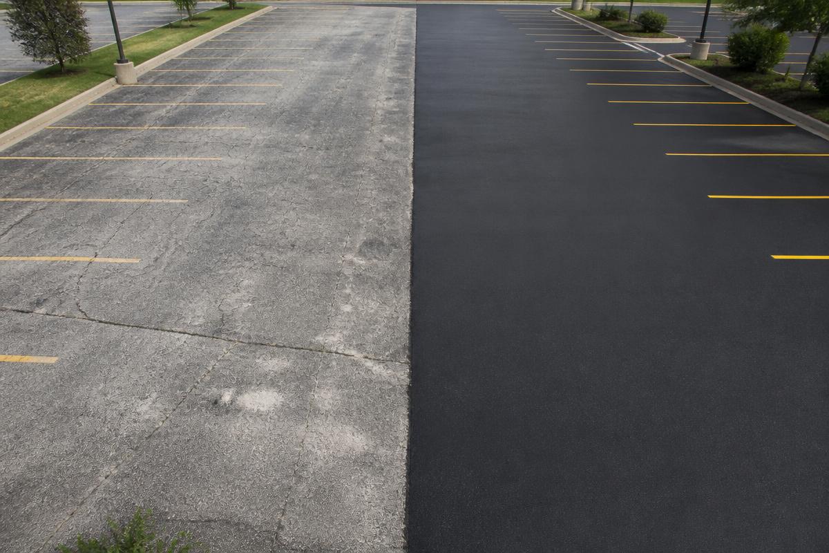 Parking lot half faded gray asphalt and half freshly sealcoated black asphalt